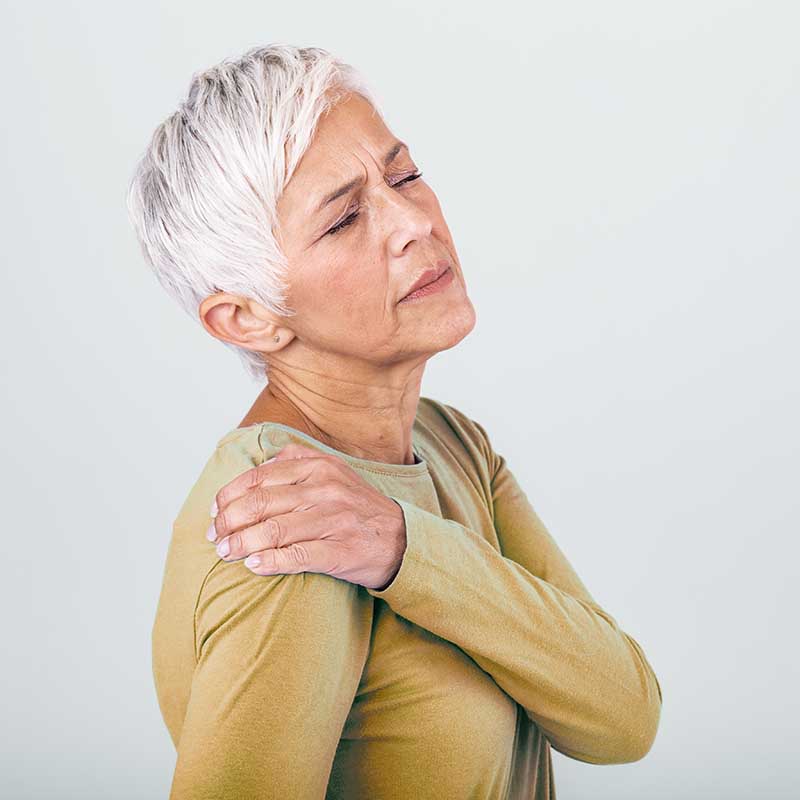 Ältere Frau hält ihre schmerzende Schulter, Schmerzen in diesem Bereich könnten auf eine Kalkschulter hindeuten.