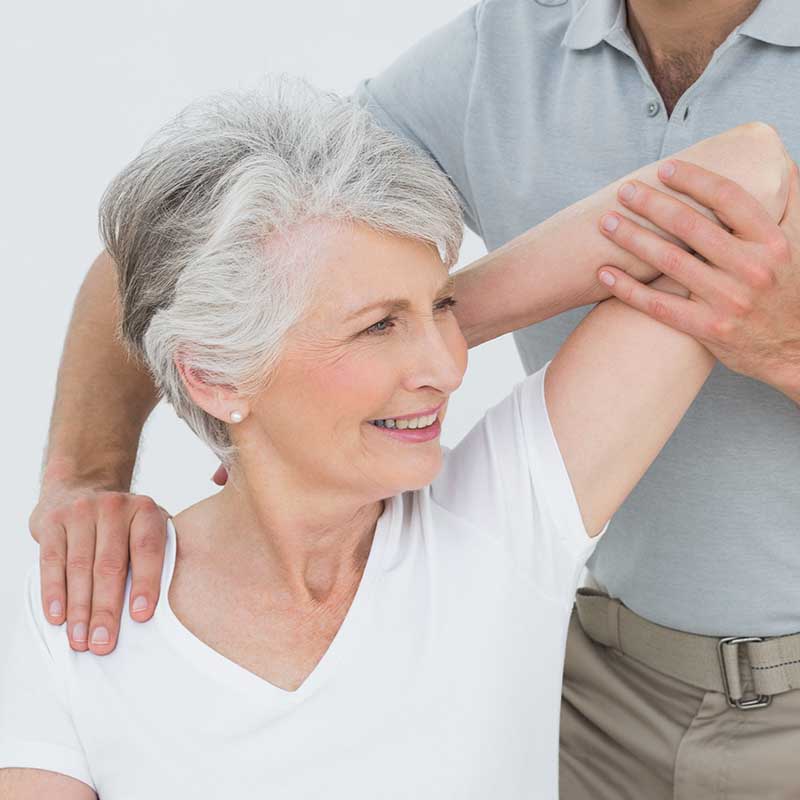 Schulter einer älteren Frau wird von einem Physiotherapeuten untersucht, möglicherweise nach einer Behandlung mit Stoßwellen bei Kalkschulter. Die Frau scheint glücklich und schmerzfrei zu sein.
