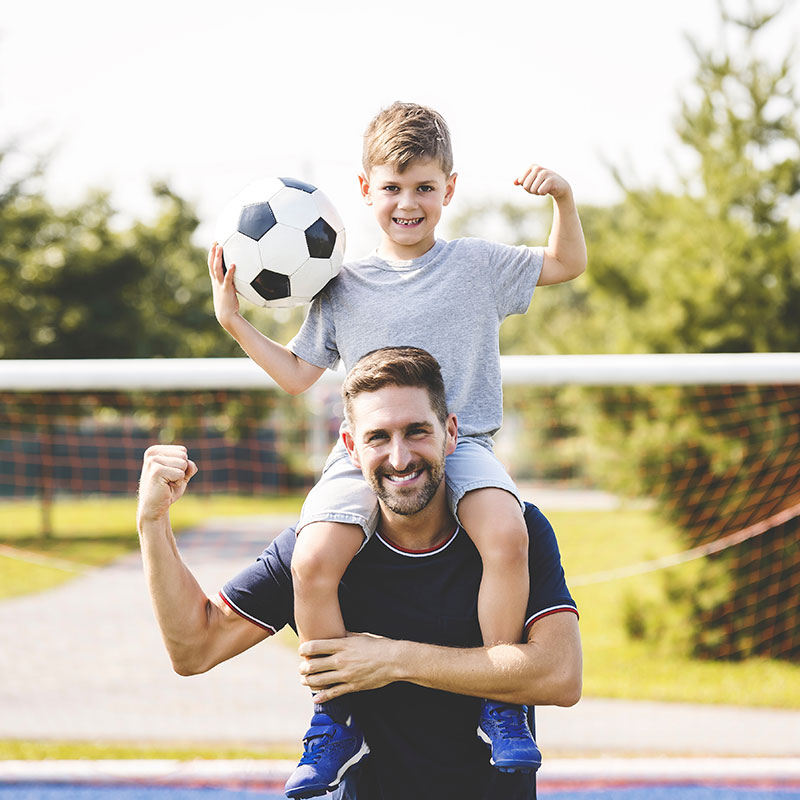 Vater und Sohn demonstrieren ihre Fitness vor einem Fußballspiel sowie die Vorteile der Stoßwellentherapie, die eine schnellere Genesung und Rückkehr zum gewohnten Alltag verspricht.