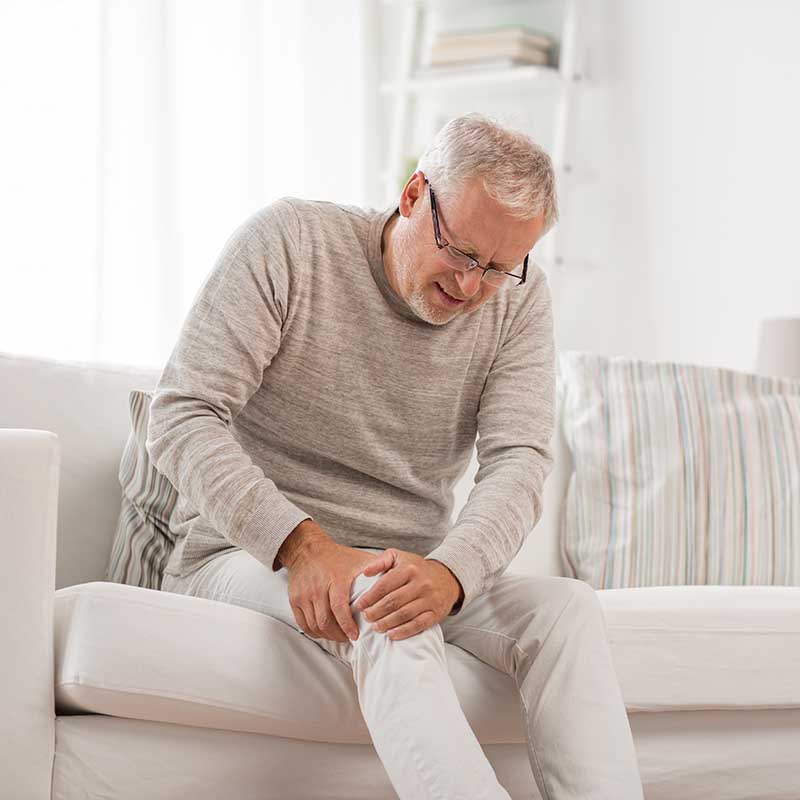 Ein älterer Mann hält sein schmerzhaftes Knie, möglicherweise auf Grund von Tendinopathie.