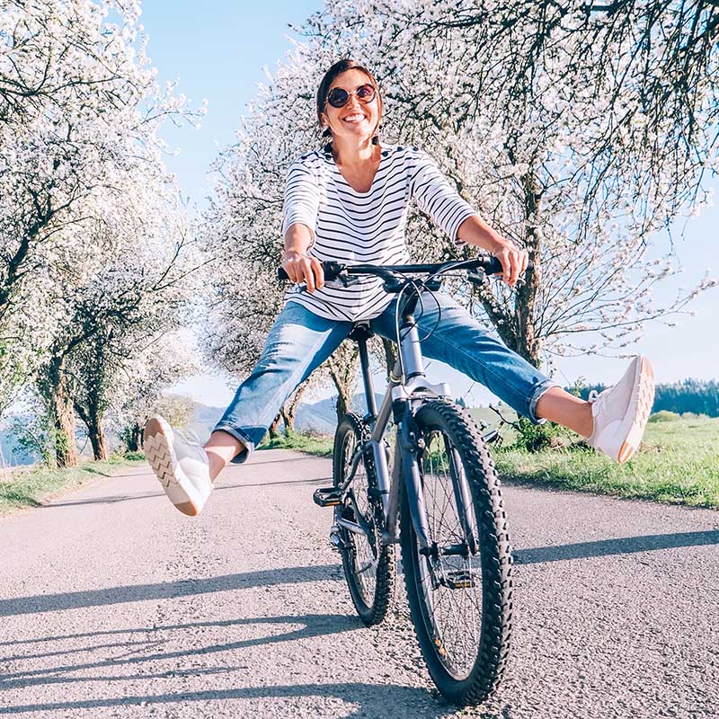 Frau beim Radfahren demonstriert ihre Fitness und die Vorteile der Stoßwellentherapie bei Tendinopathie, die eine schnellere Genesung und Rückkehr zum gewohnten Alltag verspricht.