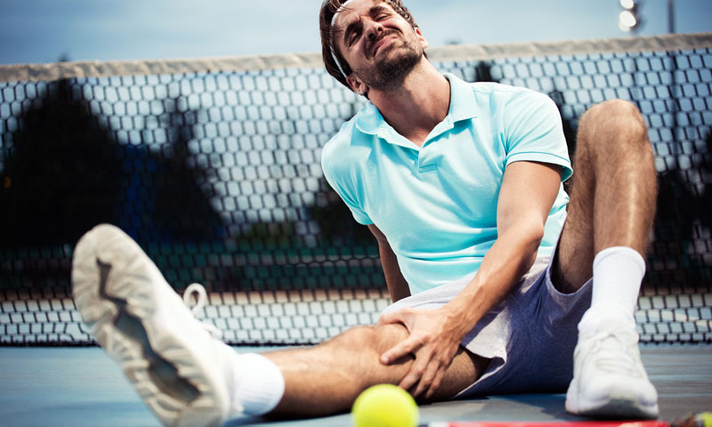 Tennisspieler sitzt am Boden und hält sich schmerzbedingt die Wade bei einer akuten Muskelverletzung
